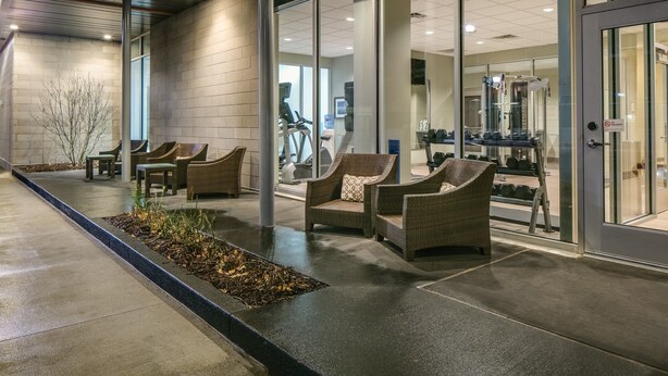 A modern building exterior with glass doors, outdoor seating, and exercise equipment. - Comfy Studio Suite | Indoor Pool, Hot Tub (Des Moines)