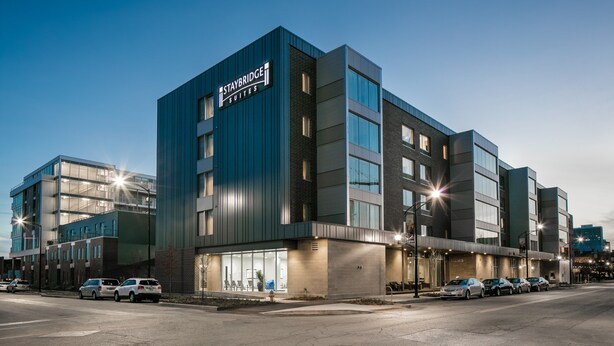 Un hôtel Staybridge Suites moderne, doté d'une enseigne bien visible, de grandes fenêtres et d'un parking où sont stationnées plusieurs voitures.