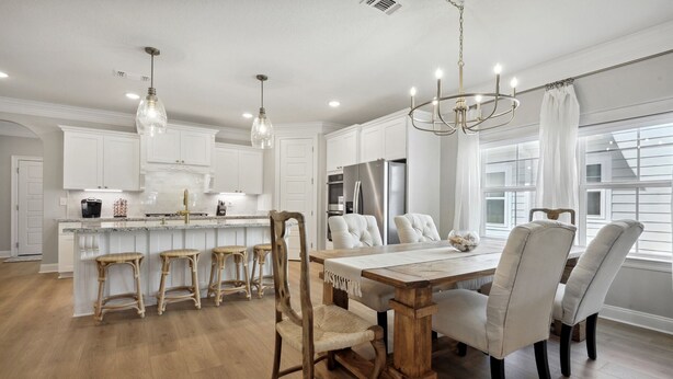 A modern kitchen with white cabinetry, a central island with stools, and a dining area with a wooden table and chairs.