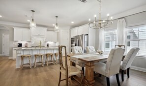 Une cuisine moderne avec des meubles blancs, un îlot central doté de tabourets et un coin repas avec une table et des chaises en bois.