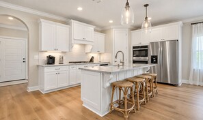 A modern kitchen with white cabinetry, a central island with bar stools, stainless steel appliances, and pendant lighting.