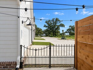 A gated entrance with a wooden fence, a clear sky, and a pathway leading to a building with a white exterior.