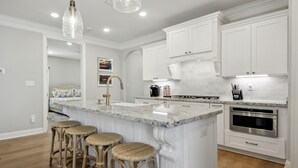 A modern kitchen with white cabinetry, a granite island with bar stools, a built-in oven, and pendant lighting.