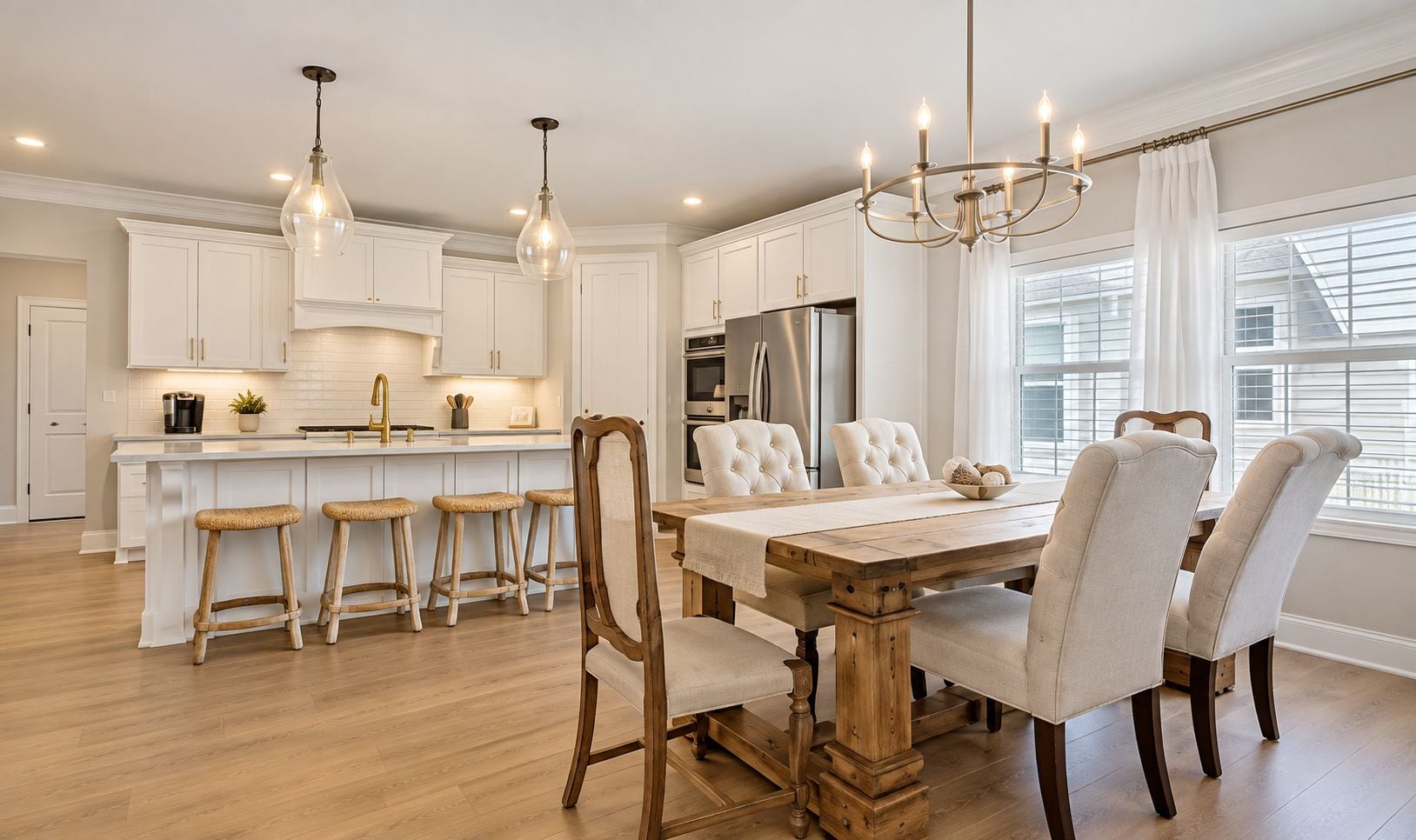 A modern kitchen with white cabinetry, a central island with stools, a dining table with chairs, and pendant lighting.