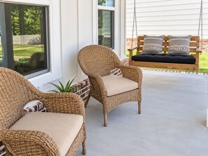 A covered porch with wicker chairs and a swing.