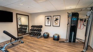 Un gimnasio con banco, mancuernas, pelotas de ejercicio y máquina de poleas.
