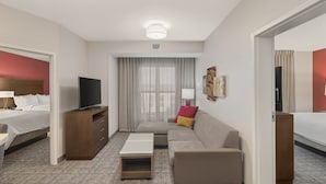 Una habitación de hotel con cama, sofá, televisión, escritorio y ventana con cortinas.