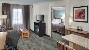 A hotel room with a bed, a desk with a computer, a TV, and a seating area with a couch and armchair. - 1 Bedroom Suite | Outdoor Pool, Free Breakfast (Ridgeland)