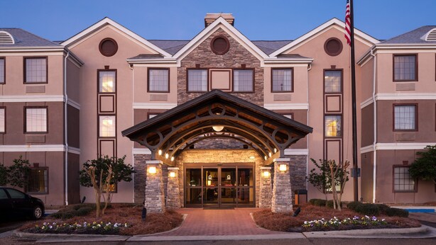 A multi-story hotel with a stone facade, large windows, and an American flag. - 1 Bedroom Suite | Outdoor Pool, Free Breakfast (Ridgeland)