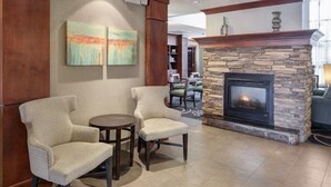 A lobby with two armchairs, a small round table, a stone fireplace, and two abstract paintings on the wall. - 1 Bedroom Suite | Outdoor Pool, Free Breakfast (Ridgeland)