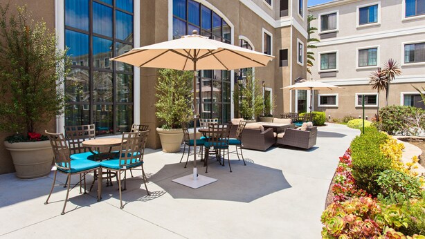 An outdoor patio area with a round table and chairs, a large umbrella, and a sofa. - Free Breakfast. Outdoor Pool & Hot Tub (Lake Forest)