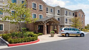 A multi-story hotel with a brick facade, large windows, and a covered entrance area with a planter. - Free Breakfast. Outdoor Pool & Hot Tub (Lake Forest)