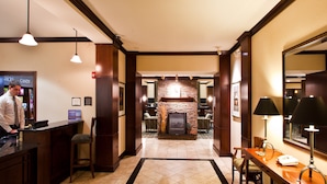 A hotel lobby with a reception desk, a stone fireplace, and a dining area with a wooden table and chairs. - 1 Bedroom | Free Breakfast. (Okemos)