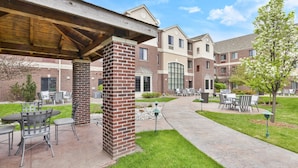 A covered patio area with outdoor seating and a brick pillar. - 1 Bedroom | Free Breakfast. (Okemos)