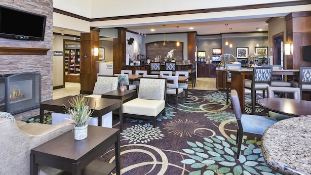 A hotel lobby with a fireplace, seating area, and a bar. - 1 Bedroom | Free Breakfast. (Okemos)
