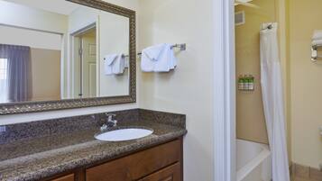A bathroom with a granite countertop sink, a mirror, and a shower area.