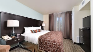A hotel room with a large bed, two bedside tables with lamps, a television, and a wardrobe. - King Suite. Free Breakfast. (Okemos)