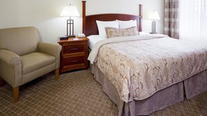 Una habitación de hotel con una cama, una silla, una mesita de noche con lámpara y un teléfono.