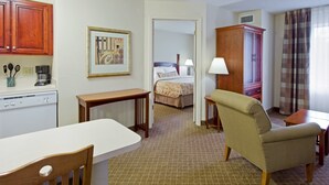 Una habitación de hotel con kitchenette, una cama, una silla, una mesa y un armario.