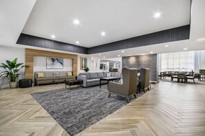 Un vestíbulo amplio con alfombra gris, pisos de madera, sofás, sillones y un comedor con mesas y sillas.