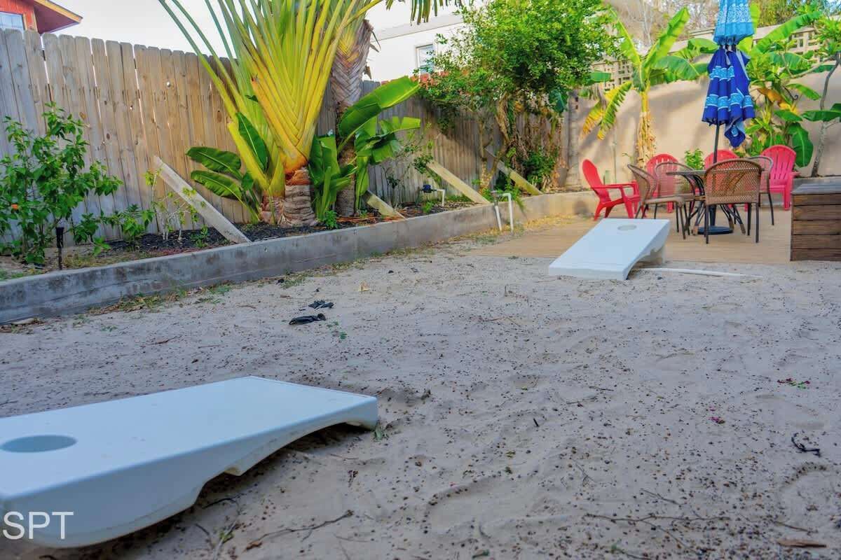 Ein sandiger Hinterhof mit einer weißen Liege, einem kleinen Tisch und roten Stühlen.