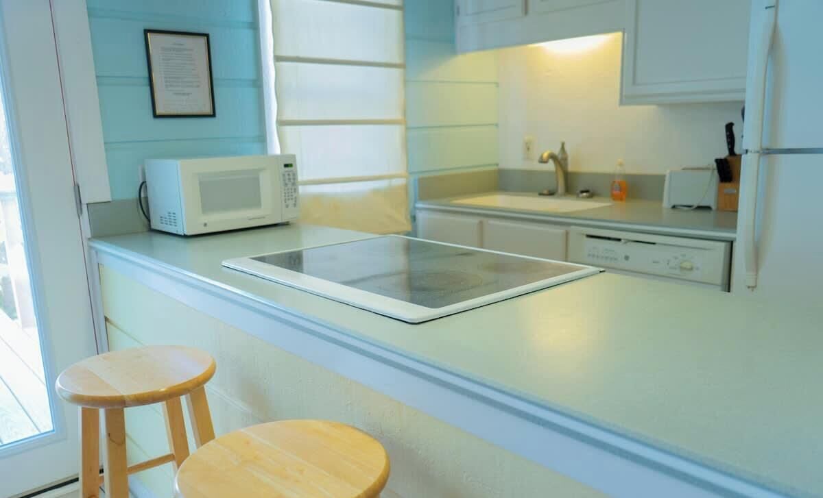Una cocina moderna con microondas, una mesa de vidrio y taburetes de madera.