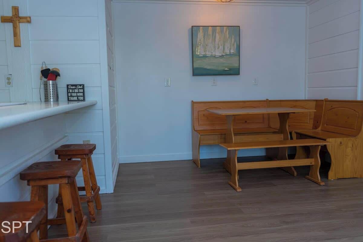 Una habitación con un banco de madera, una mesita y una estantería con una cruz y un cartel.
