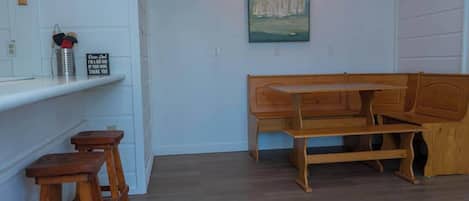 Una habitación con un banco de madera, una mesita y una estantería con una cruz y un cartel.