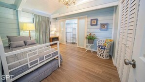 A bedroom with a bunk bed, a small table with a chair, a chandelier, and a view through an open door. - Warm Vibes - 5 Mins to Beach - Cool Retro Feel (South Padre Island)
