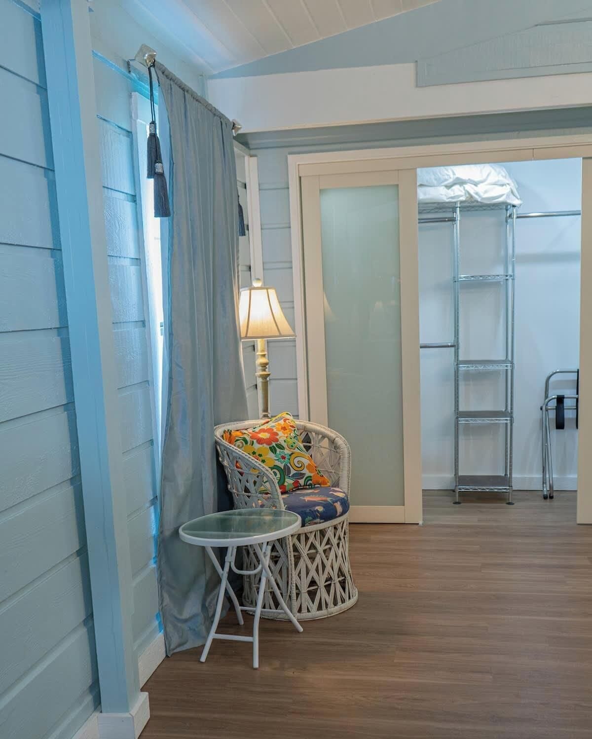 A room with a wicker chair, a small table, a lamp, and a ladder against a wall.