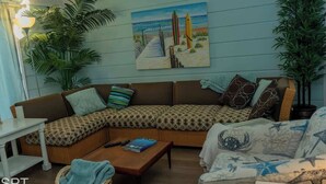 A cozy living room with a sectional sofa, a coffee table, and a painting of a beach scene. - Warm Vibes - 5 Mins to Beach - Cool Retro Feel (South Padre Island)