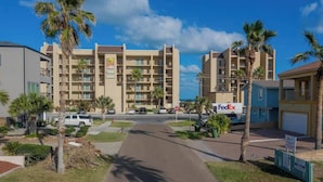 A multi-story hotel with a central courtyard, palm trees, and a FedEx sign. - Warm Vibes - 5 Mins to Beach - Cool Retro Feel (South Padre Island)