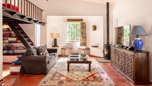 Ein gemütliches Wohnzimmer mit einer Couch, einem Couchtisch und einem Kamin. Eine Treppe führt zu einer Erkeretage mit Bücherregalen.