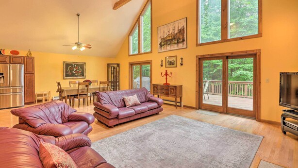 A spacious living room with a large sofa, a dining area, and a balcony with a view of the outdoors. - Fire Pit, Indoor Pool Access: Big Bass Lake Cabin (Clifton Township)