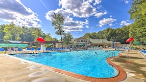 A swimming pool with blue water, surrounded by lounge chairs and umbrellas. - Fire Pit, Indoor Pool Access: Big Bass Lake Cabin (Clifton Township)