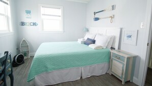 Un dormitorio con una cama, mesita de noche, cómoda, silla, ventilador y ventana.