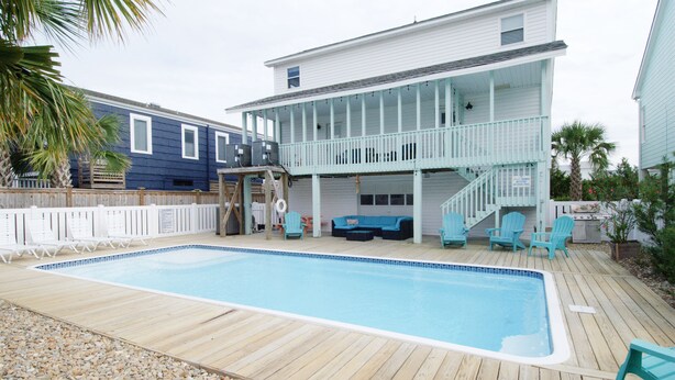 Una casa de dos pisos con piscina y zona de estar exterior.