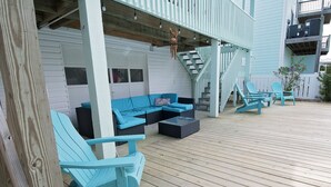 Una terraza techada con sillas Adirondack azules, un sofá y una escalera que sube a un nivel superior.