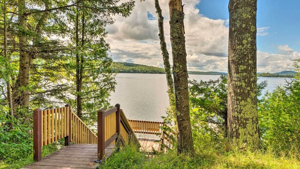 A wooden bridge leading to a dock over a calm lake, surrounded by trees and greenery. - Rustic Cabin Retreat on Rangeley Lake! (Rangeley)