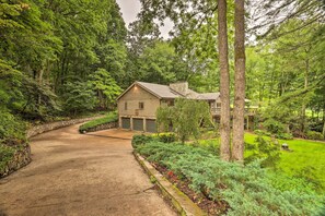 A house with a stone chimney, surrounded by lush greenery and a curved driveway.