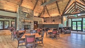 A spacious indoor area with wooden floors, stone walls, and a stone fireplace. Tables and chairs are arranged for dining or socializing. - 'Cold Mountain Reflections' Cabin w/ Game Room! (Canton)