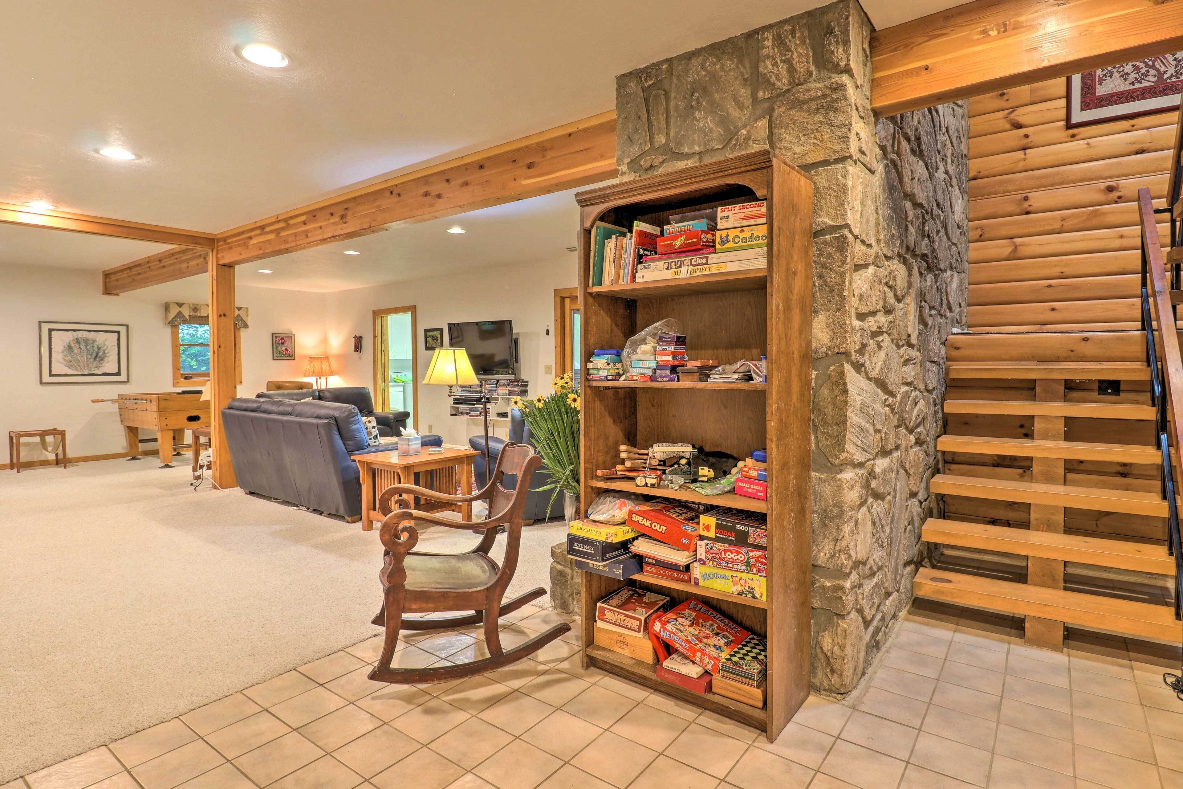A cozy living area with a wooden bookshelf filled with board games, a rocking chair, and a stone wall.