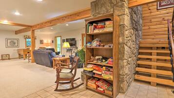 A cozy living area with a wooden bookshelf filled with board games, a rocking chair, and a stone wall.