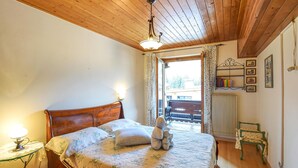 A bedroom with a wooden ceiling, a bed with floral bedding, a nightstand with a lamp, a window with curtains, and a radiator. - Amazing apartment in Racines/Ratschings (Racines/Ratschings)