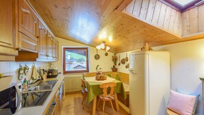 A compact kitchen with wooden cabinets, a dining table with chairs, a refrigerator, and a window offering a view of a building. - Amazing apartment in Racines/Ratschings (Racines/Ratschings)