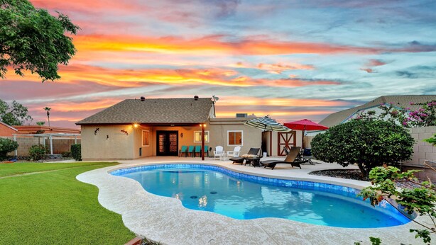 A backyard with a swimming pool, a house, and a patio area with chairs and an umbrella. - Spring Training, Heated Pool, Big Yard, Grill, Quiet Neighborhood (Peoria)