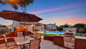 An outdoor patio with a table and chairs, a grill, and a pool in the background. - Spring Training, Heated Pool, Big Yard, Grill, Quiet Neighborhood (Peoria)