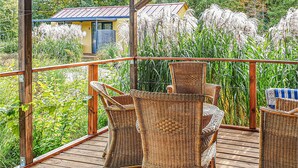 A wooden deck with wicker furniture and a view of a house and tall grasses. - Beautiful home in Biskupiec with lake view (Biskupiec)