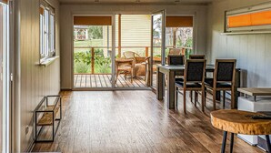 A room with a wooden floor, a dining table with chairs, a small round table, and a view of a garden through a sliding glass door. - Beautiful home in Biskupiec with lake view (Biskupiec)