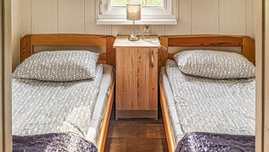 A small, cozy room with two single beds, a wooden nightstand with a lamp, and a window with a view of trees. - Beautiful home in Biskupiec with lake view (Biskupiec)